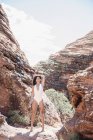 Young woman in white swimsuit standing in canyon valley with arm raised. — Stock Photo