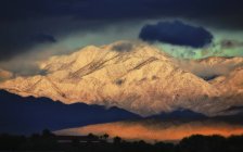 Snow-covered slopes of mountain range with dark stormy sky in valley. — Stock Photo