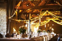 Wedding venue decorated for party with fairy lights and table set for dinner. — Stock Photo
