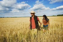 Man and woman holding hands while walking through field in summer. — Stock Photo