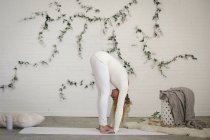 Femme blonde se penchant vers l'avant sur tapis de yoga blanc . — Photo de stock