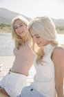Portrait of two blonde sisters sitting on lake jetty. — Stock Photo