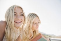 Two blonde sisters lying on jetty and reading book. — Stock Photo
