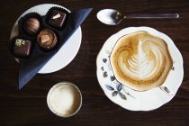 Sortierte handgemachte Schokoladenbonbons auf Teller mit Tasse Kaffee mit Schaumstoffmuster. — Stockfoto