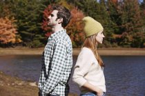 Couple standing back to back by countryside lake. — Stock Photo