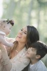 Lächelnde Mutter trägt Baby-Mädchen mit Blumenkranz mit Sohn ins Freie. — Stockfoto