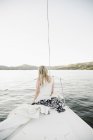 Blonde teenage girl sitting on sailboat bow at lake. — Stock Photo