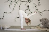 Mulher loira de couro branco e leggings curvando-se e esticando-se no tapete de ioga . — Fotografia de Stock