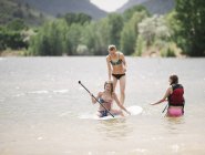 Teenage girls stand up paddle surfing on lake water. — Stock Photo