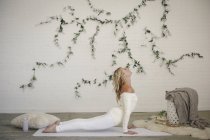 Mujer rubia acostada en una esterilla blanca y haciendo pose de yoga para perros orientada hacia arriba . - foto de stock