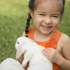 Preschooler girl holding white rabbit outdoors. — Stock Photo