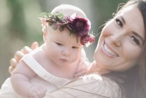 Glückliche Mutter hält Baby-Mädchen mit Blumenkranz. — Stockfoto