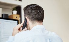 Задний вид человека разговаривающего по телефону и смотрящего на монитор компьютера . — стоковое фото