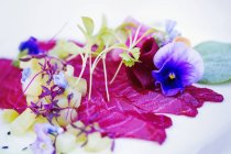 Carpaccio and garnish of fresh pea shoots and edible flowers on white plate. — Stock Photo