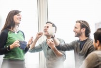 Colleagues laughing and raising coffee cups at break. — Stock Photo