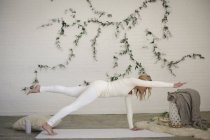Frau auf weißer Yoga-Matte mit erhobenem Bein und ausgestrecktem Arm. — Stockfoto