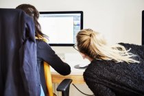 Dos mujeres compartiendo computadora y discutiendo gráficos en pantalla . - foto de stock