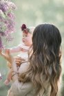 Mère tenant bébé fille avec couronne de fleurs dans le jardin . — Photo de stock