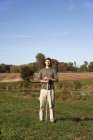 Взрослый мужчина, стоящий в поле и держащий садовый инструмент . — стоковое фото