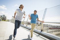 Zwei junge Männer joggen über Stadtbrücke. — Stockfoto
