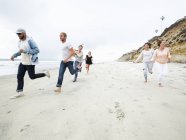 Gruppo di giovani uomini e donne che corrono sulla spiaggia e si divertono . — Foto stock