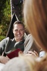 Man smiling and looking in camera while sitting with woman in hammock. — Stock Photo