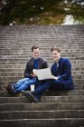 Two young men sitting on steps in city and using laptop together. — Stock Photo