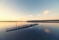 Дерев'яні dock плаваючий на плоскі спокійна вода озеро на заході сонця. — стокове фото