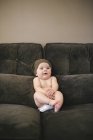 Baby sitzt in Windel und Strickmütze auf Sofa. — Stockfoto