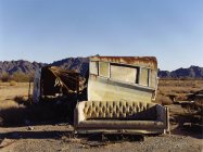 Ruined caravan with rusting roof with old sofa in desert. — Stock Photo