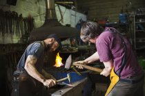 Two blacksmiths hammering piece of metal on anvil in workshop. — Stock Photo
