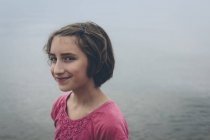 Retrato de menina pré-adolescente sorridente em frente à água do lago . — Fotografia de Stock