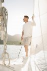 Mature man standing on sailboat and holding on sail at lake. — Stock Photo