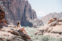 Young woman in white swimsuit resting on rocks in canyon valley with arm raised. — Stock Photo