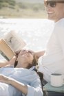 Woman resting on lap of reclining man with book on jetty. — Stock Photo