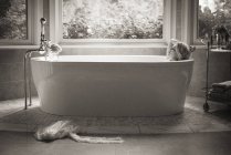Woman lying in free-standing bathtub in bathroom with large window. — Stock Photo