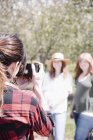 Visão traseira de fotógrafa feminina tirando fotos de mulheres no pomar no verão . — Fotografia de Stock