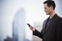 Молодий бізнесмен стоїть на даху і дивиться вниз на смартфон . — стокове фото