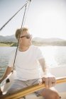 Mature man in sunglasses relaxing and steering sailboat on lake. — Stock Photo