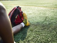 Männerbeine in gelben Sportschuhen auf grünem Rasen mit Rucksack am Fuß. — Stockfoto