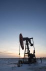 Equipamento de perfuração de petróleo e pumpjack na planície plana no campo de petróleo canadense ao pôr-do-sol . — Fotografia de Stock