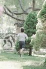 Rear view of elementary age boy running across lawn in garden. — Stock Photo
