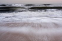 Waves crashing on sandy beach in motion blur. — Stock Photo