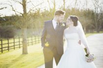 Bride and groom walking down path in soft light outdoors. — Stock Photo