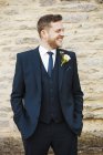 Bräutigam im Anzug mit Blume im Knopfloch und Händen in Taschen, die draußen lächeln. — Stockfoto