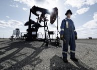 Чоловік в комбінезоні і жорсткий капелюх на гнізді насоса у відкритому грунті на місці видобутку нафти . — стокове фото
