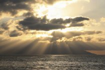 Eixos de luz solar através de nuvens caindo na água do oceano — Fotografia de Stock