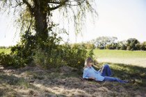 Жінка відпочиває відтінок дерева в сільськогосподарському ландшафті і читає книгу . — стокове фото