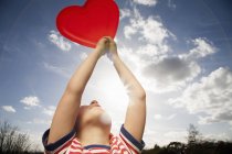 Low angle view of child holding red heart shape outdoors. — Stock Photo
