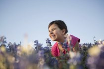 Menina pré-adolescente sentado no campo de grama alta e flores silvestres azuis . — Fotografia de Stock